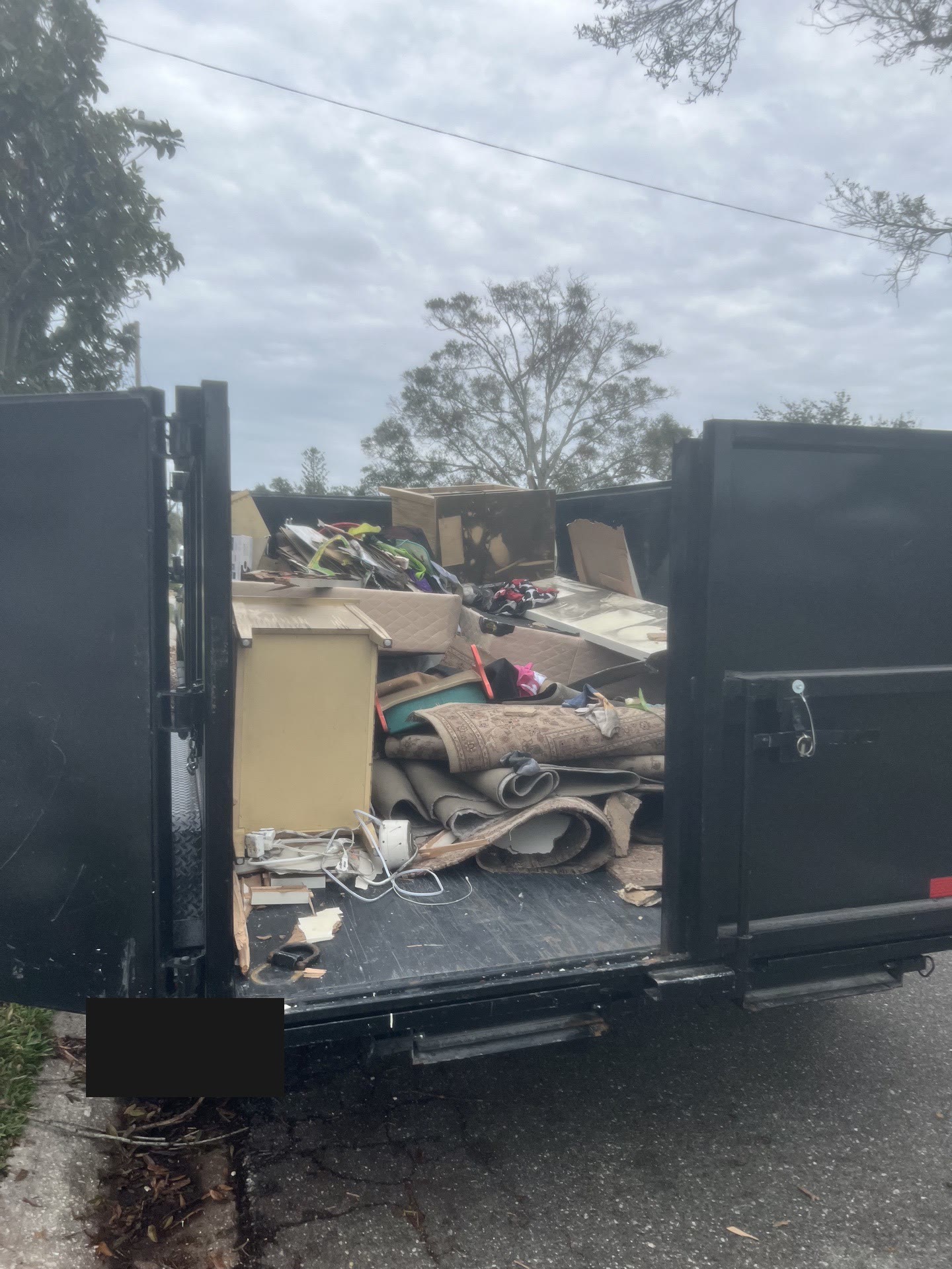 Dump trailer with rear barn doors open, fully loaded with household debris from an estate cleanout.