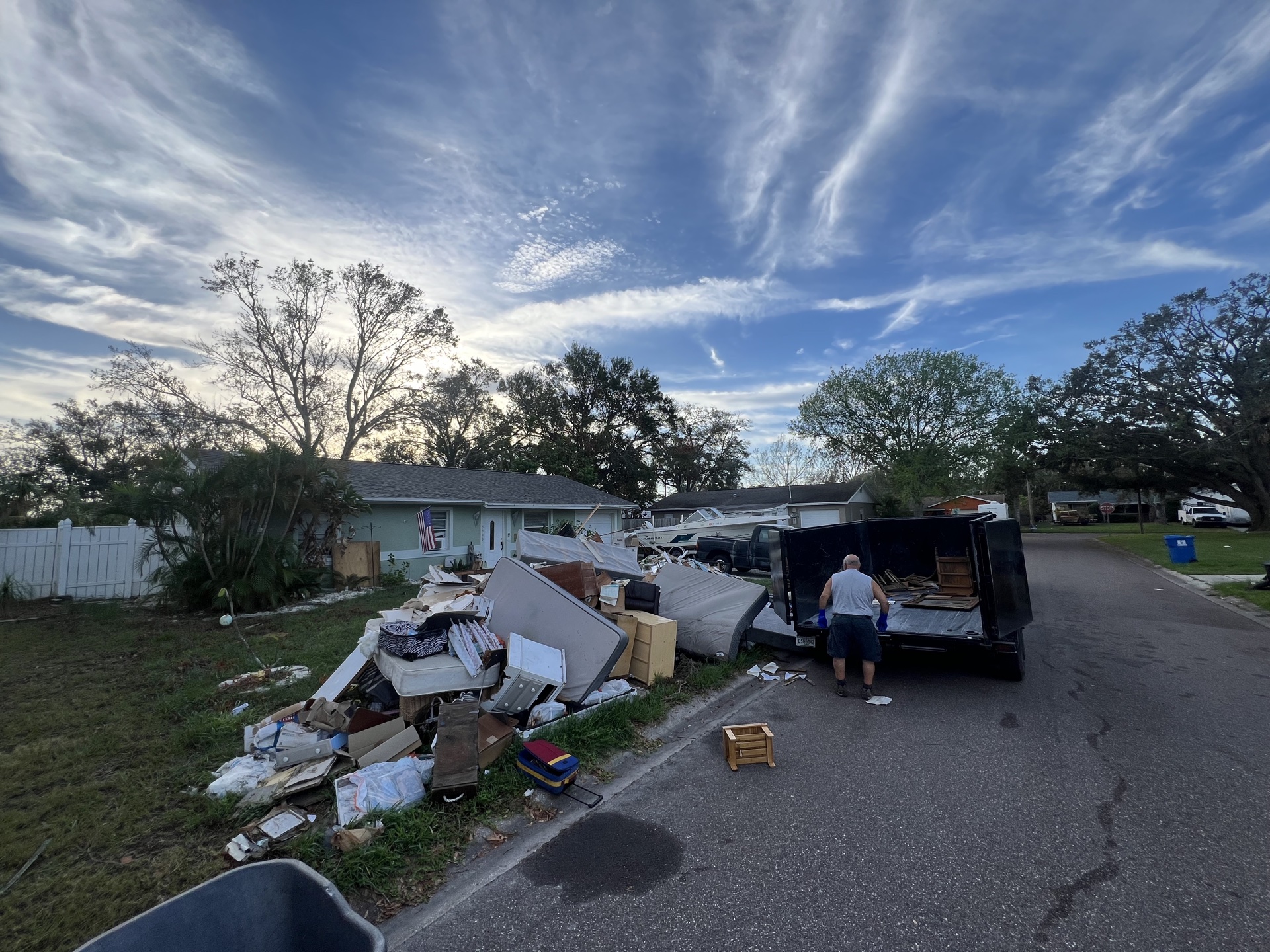 Curbside cleanup in St. Petersburg, large debris pile being loaded into the dump trailer at sunset.